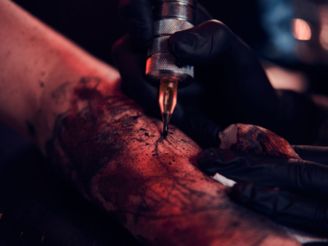 Closeup photo shoot of tattoo making, artist is working with tattoo machine on customer's hand.